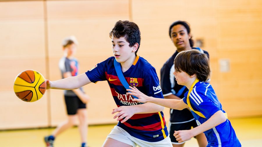 Schüler*innen, die beim Sportunterricht Basketball spielen
