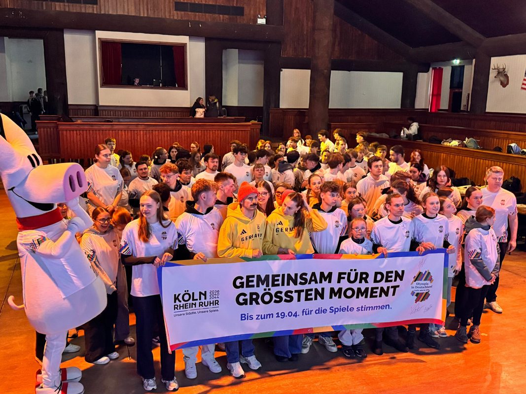 Teilnehmende und Olympioniken halten Banner "Gemeinsam für den größten Moment"