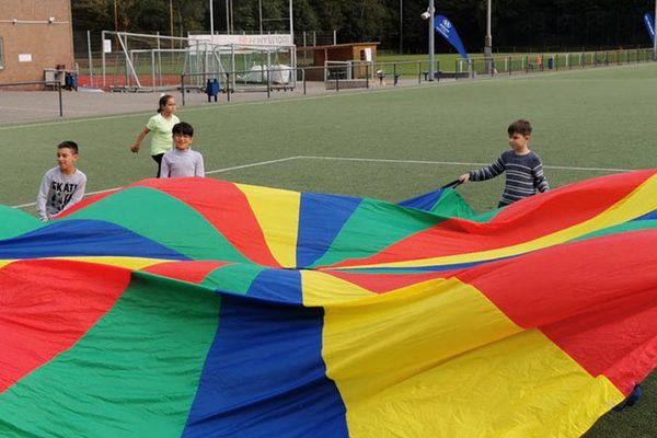 Kinder spielen mit dem Schwungtuch auf Sportplatz