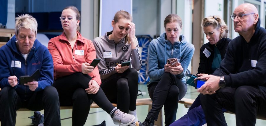 sechs Menschen auf einer Bank mit Handys in der Hand