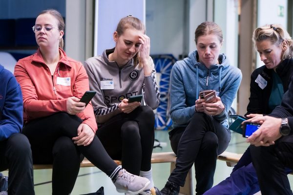 sechs Menschen auf einer Bank mit Handys in der Hand