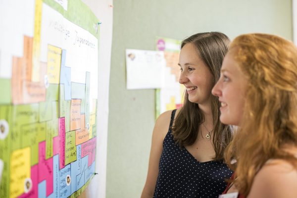 zwei junge Frauen, die sich Infos an einer Wand anschauen 