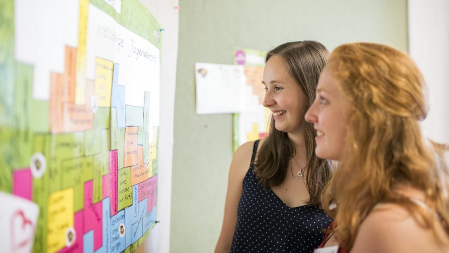 zwei junge Frauen, die sich Infos an einer Wand anschauen 